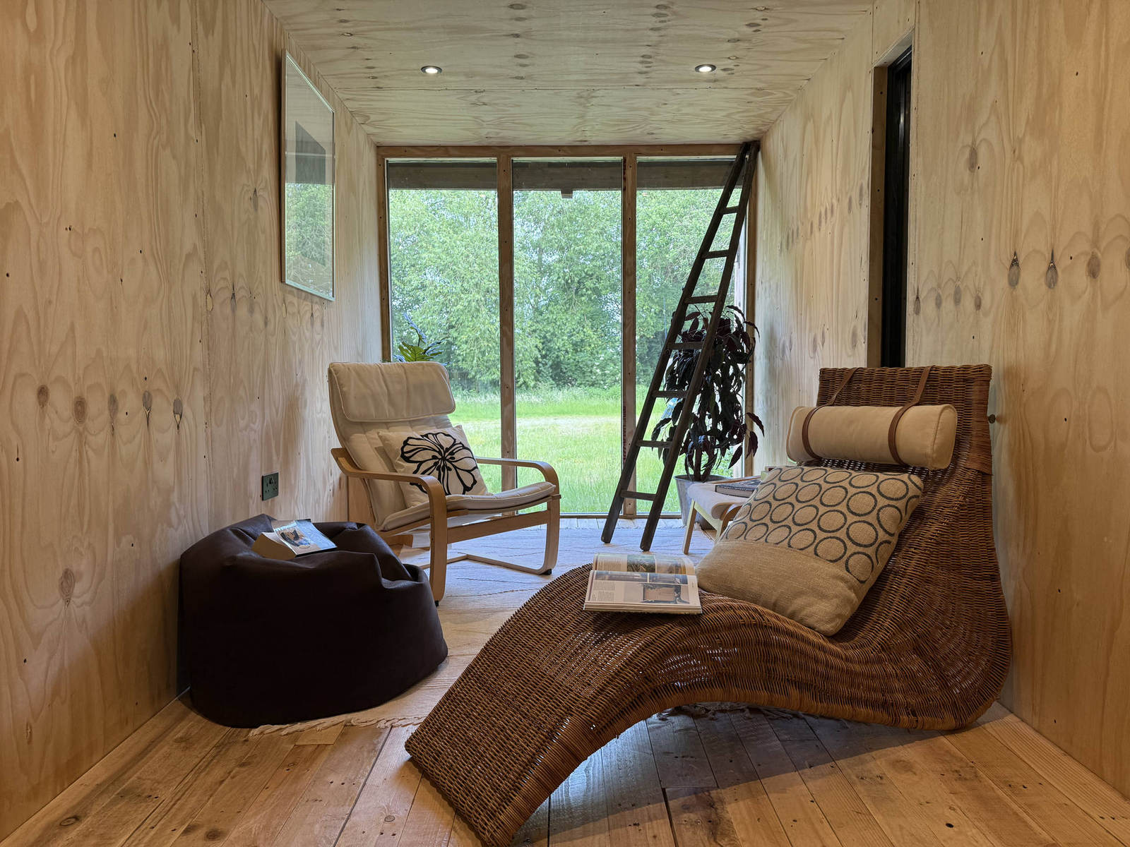 Corva interior — living space with wicker chaise and glazing onto open meadow